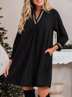 Woman wearing a black dress with decorative trim in a festive indoor setting.