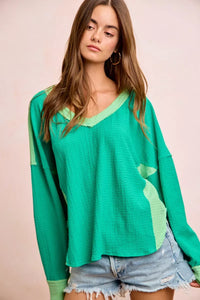 Woman wearing a green long-sleeve top with a pink background