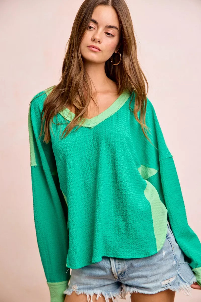 Woman wearing a green long-sleeve top with a pink background
