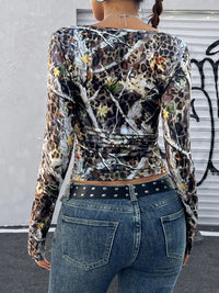 Person wearing a camouflage and leopard print long-sleeve top with blue jeans.