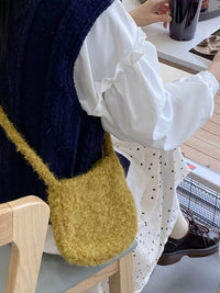 Person wearing a mustard yellow bag with a white shirt and dark sweater, sitting at a table.