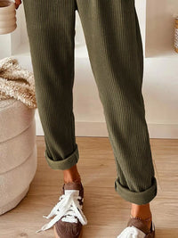 Person wearing green ribbed pants with white sneakers in a home setting