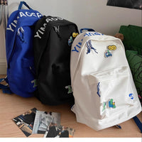 Three backpacks in blue, black, and white with various designs on a wooden floor.