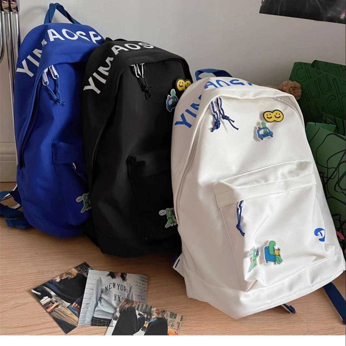 Three backpacks in blue, black, and white with various designs on a wooden floor.