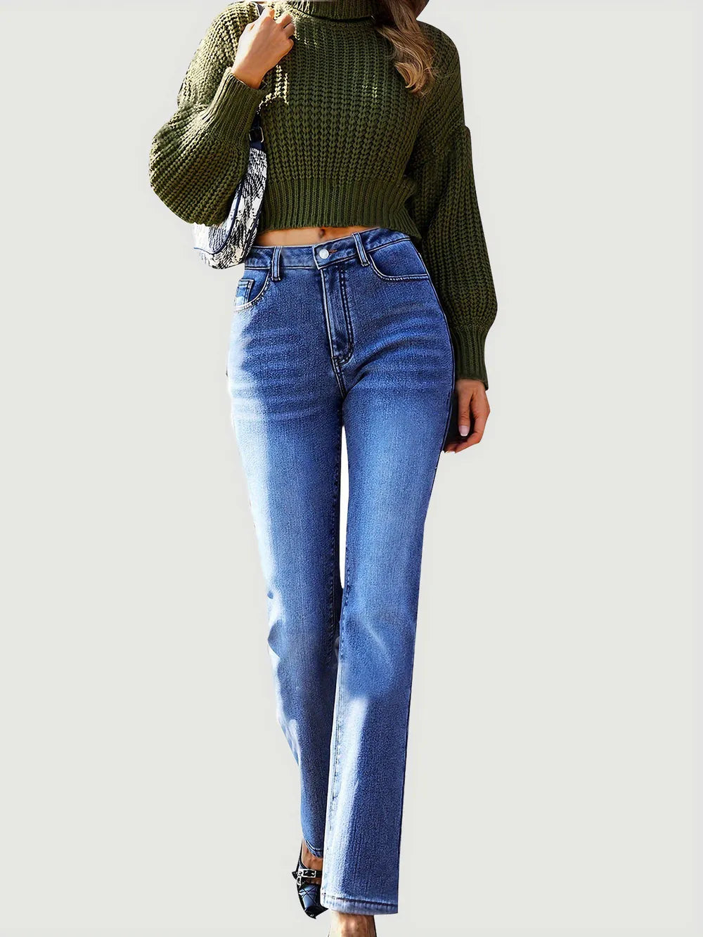 Person wearing a green knitted sweater and blue jeans on a white background
