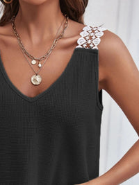 Person wearing a black sleeveless top with layered necklaces and earrings.