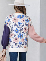 Person wearing a floral-patterned sweater with blue and pink flowers on a plain background