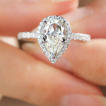 Teardrop-shaped diamond ring on a finger with a blurred background