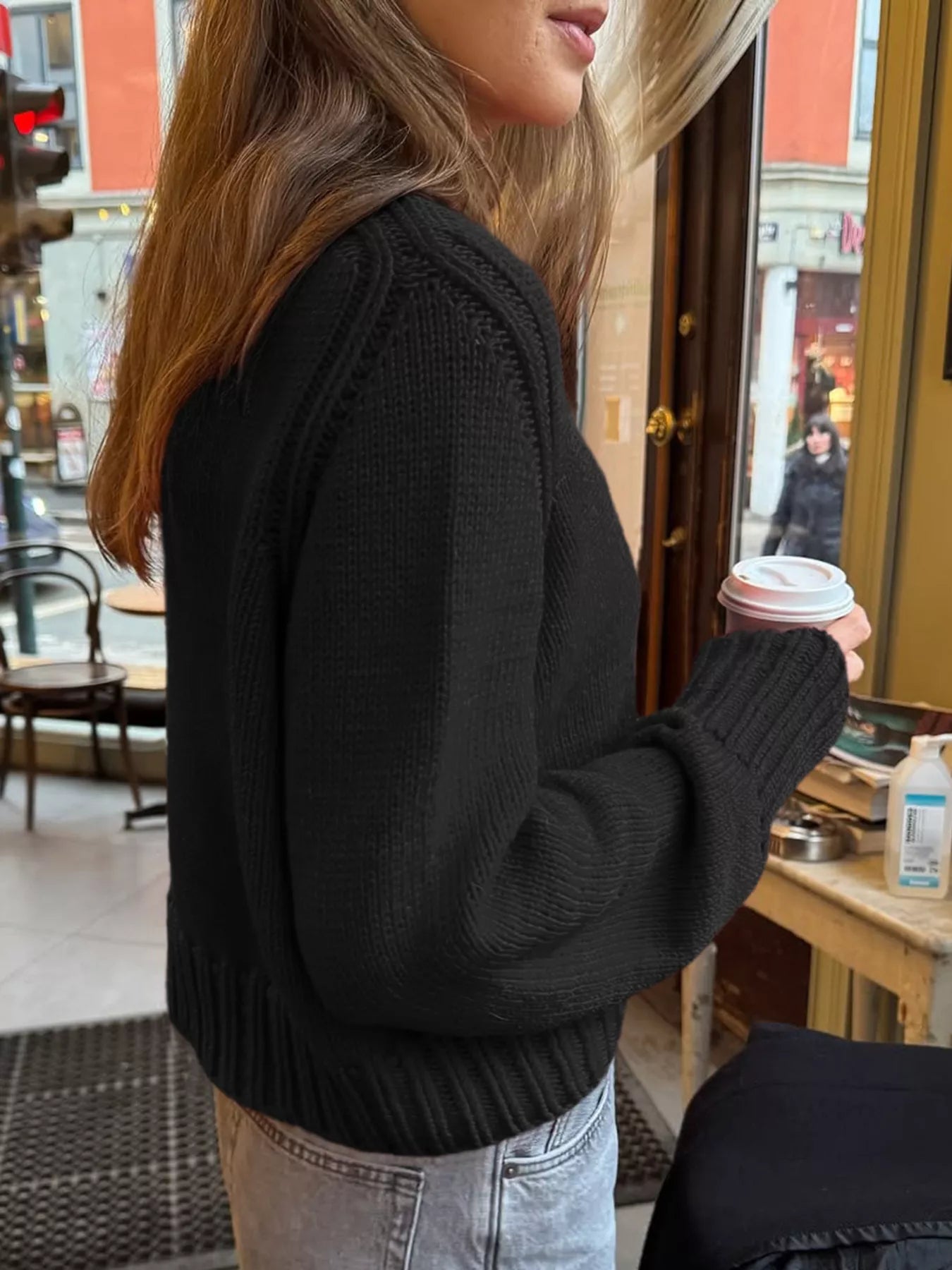 Person wearing a black sweater holding a coffee cup in an indoor setting