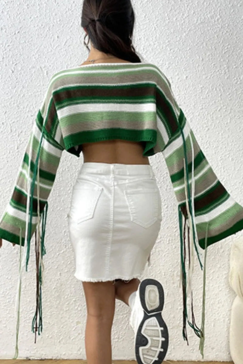 Person wearing a green and brown striped poncho over a white skirt against a plain background