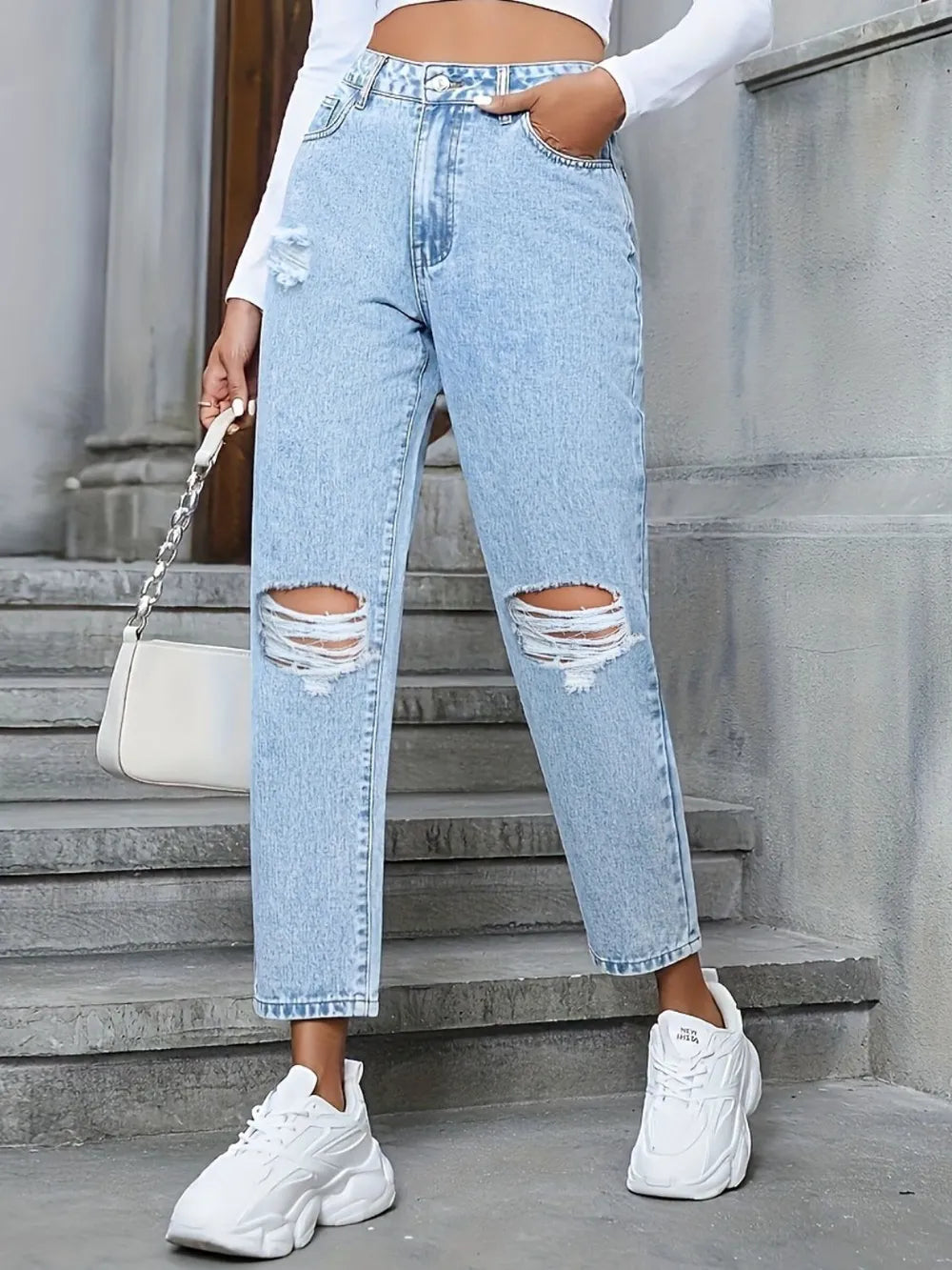 Person wearing light blue ripped jeans and white sneakers standing on stone steps.