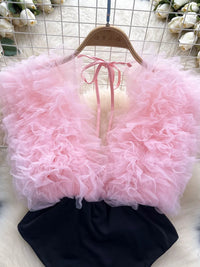 Pink ruffled top and black shorts on a hanger with white flowers in the background