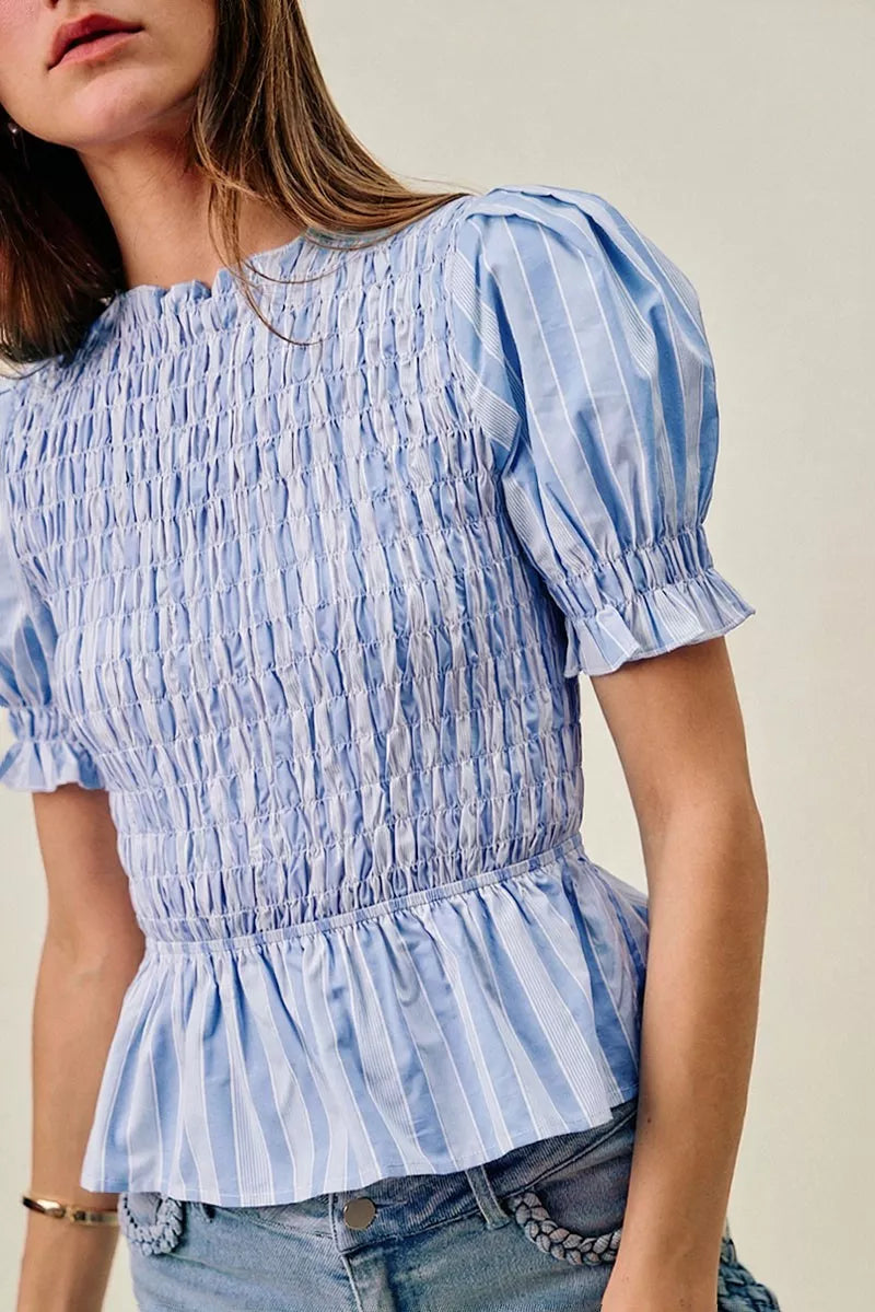 Woman wearing a blue and white striped blouse with ruffled details.