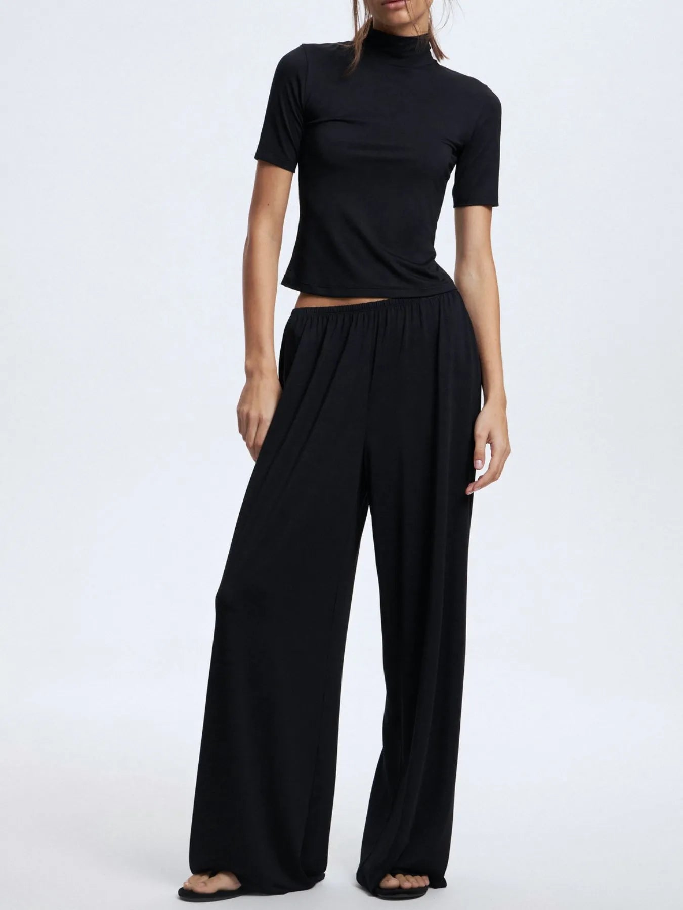 Person wearing a black outfit with a top and wide-leg pants on a white background