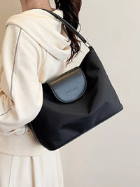 Person holding a black handbag with a visible brand logo against a plain background