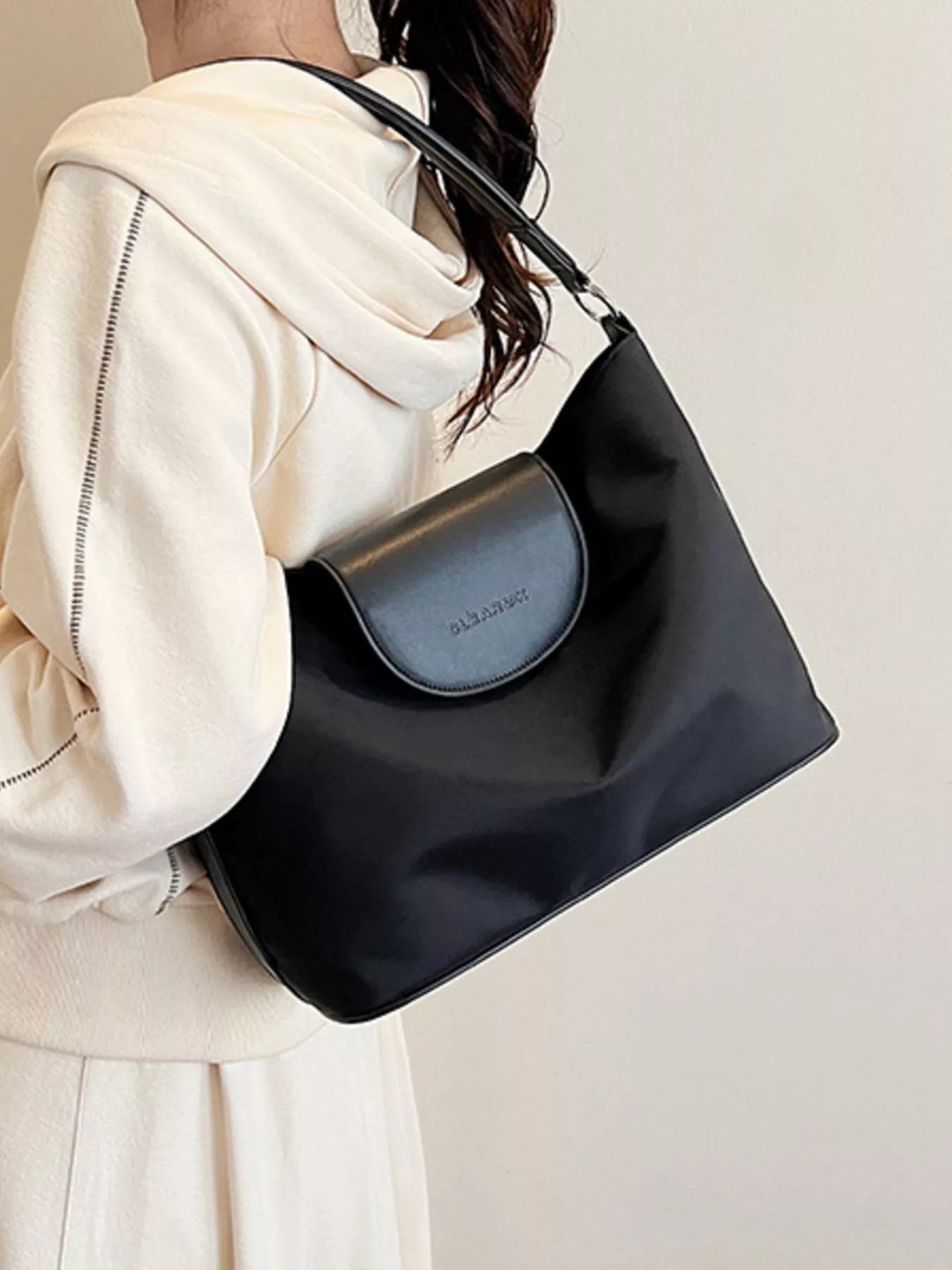 Person holding a black handbag with a visible brand logo against a plain background