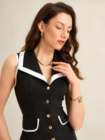 Woman wearing a black dress with white trim and gold buttons against a beige background