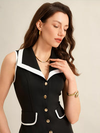 Woman wearing a black dress with white trim and gold buttons against a beige background