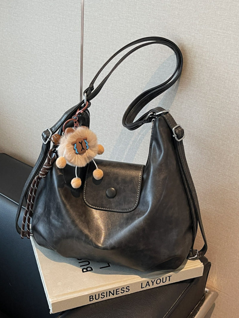 Black handbag with a fluffy keychain on a stack of books against a neutral background