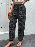 Person wearing black patterned pants against a white wall.