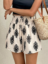 Person wearing a white skirt with black patterns and a black top, holding a straw bag.