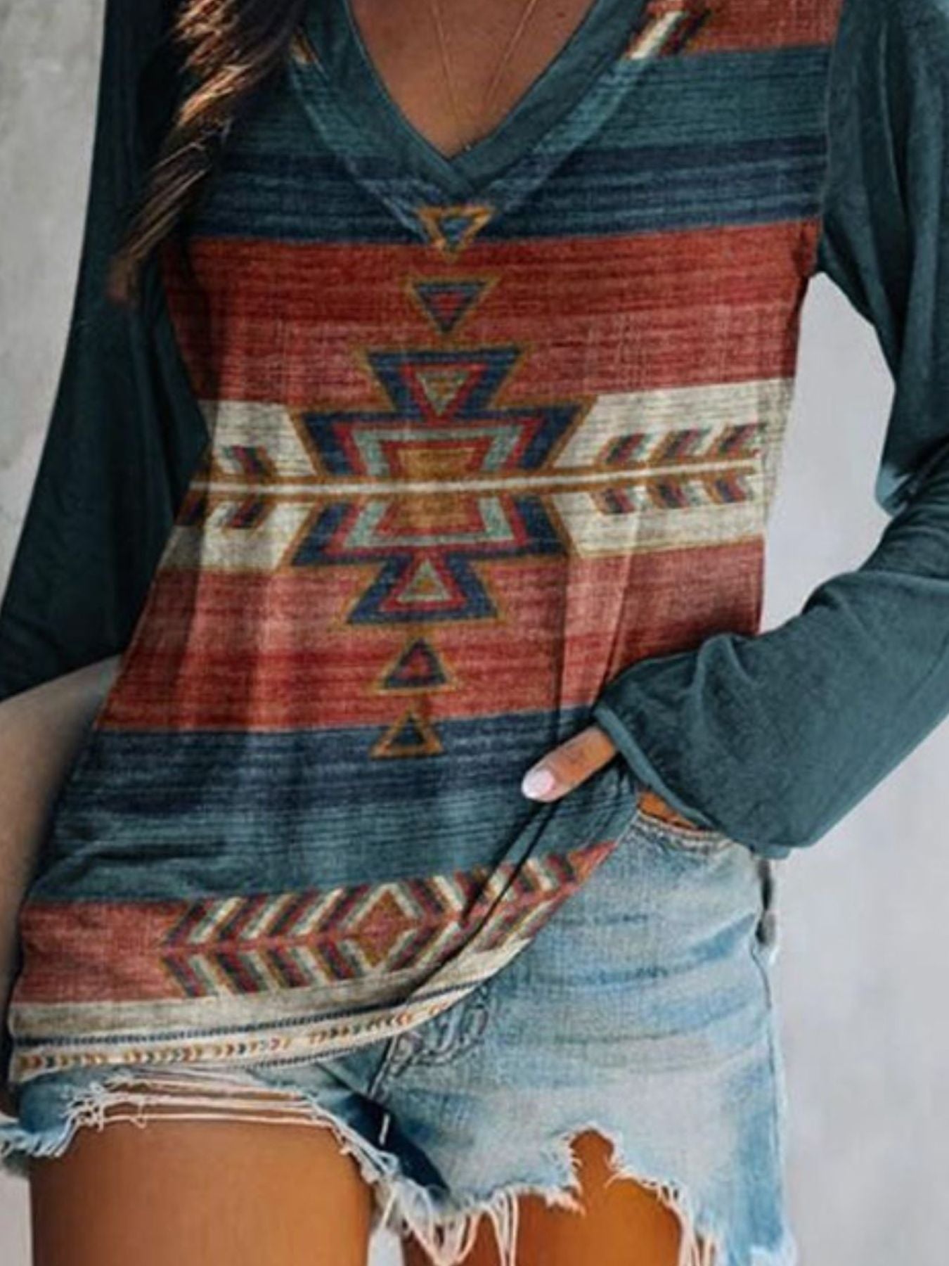 Person wearing a long-sleeve shirt with a geometric pattern and denim shorts on a plain background