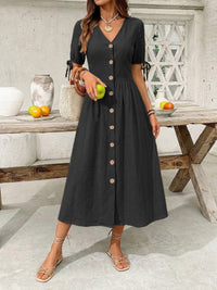 Woman wearing a black dress with buttons in an outdoor setting.