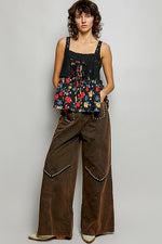 Woman wearing a floral top and brown pants against a plain background