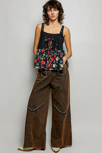 Woman wearing a floral top and brown pants against a plain background