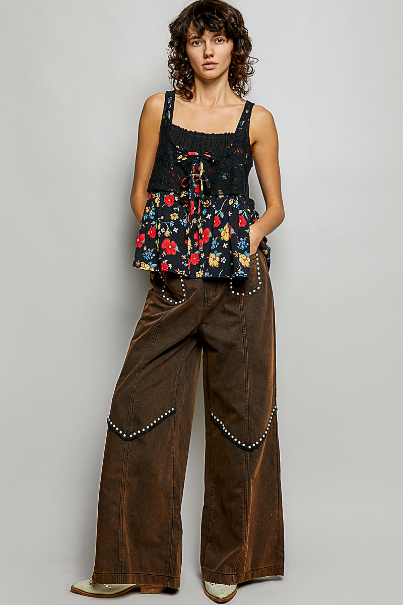 Woman wearing a floral top and brown pants against a plain background