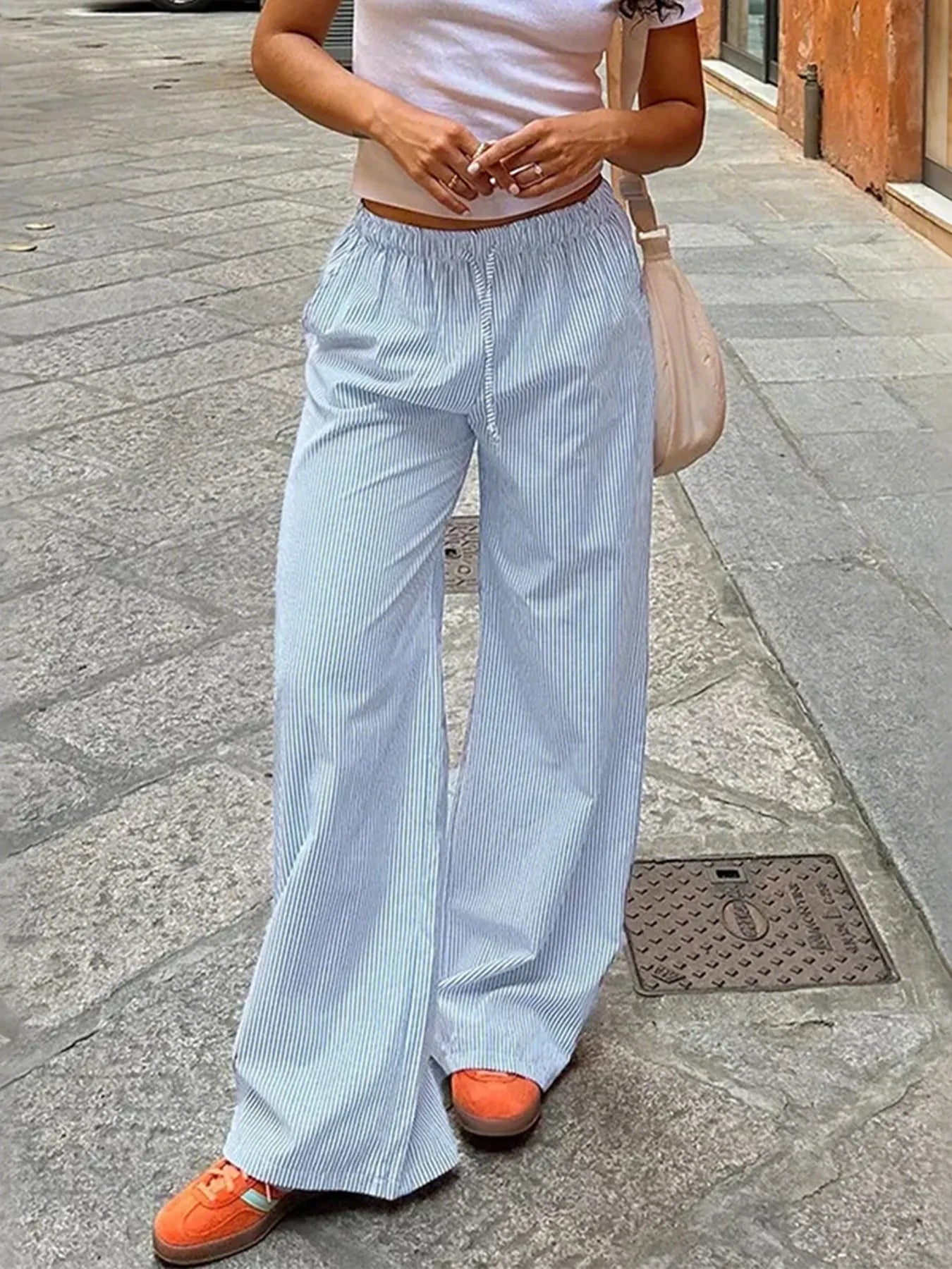 Person wearing light blue striped pants and orange shoes on a sidewalk.