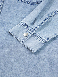 Close-up of a light blue denim shirt with a button on a matching fabric background