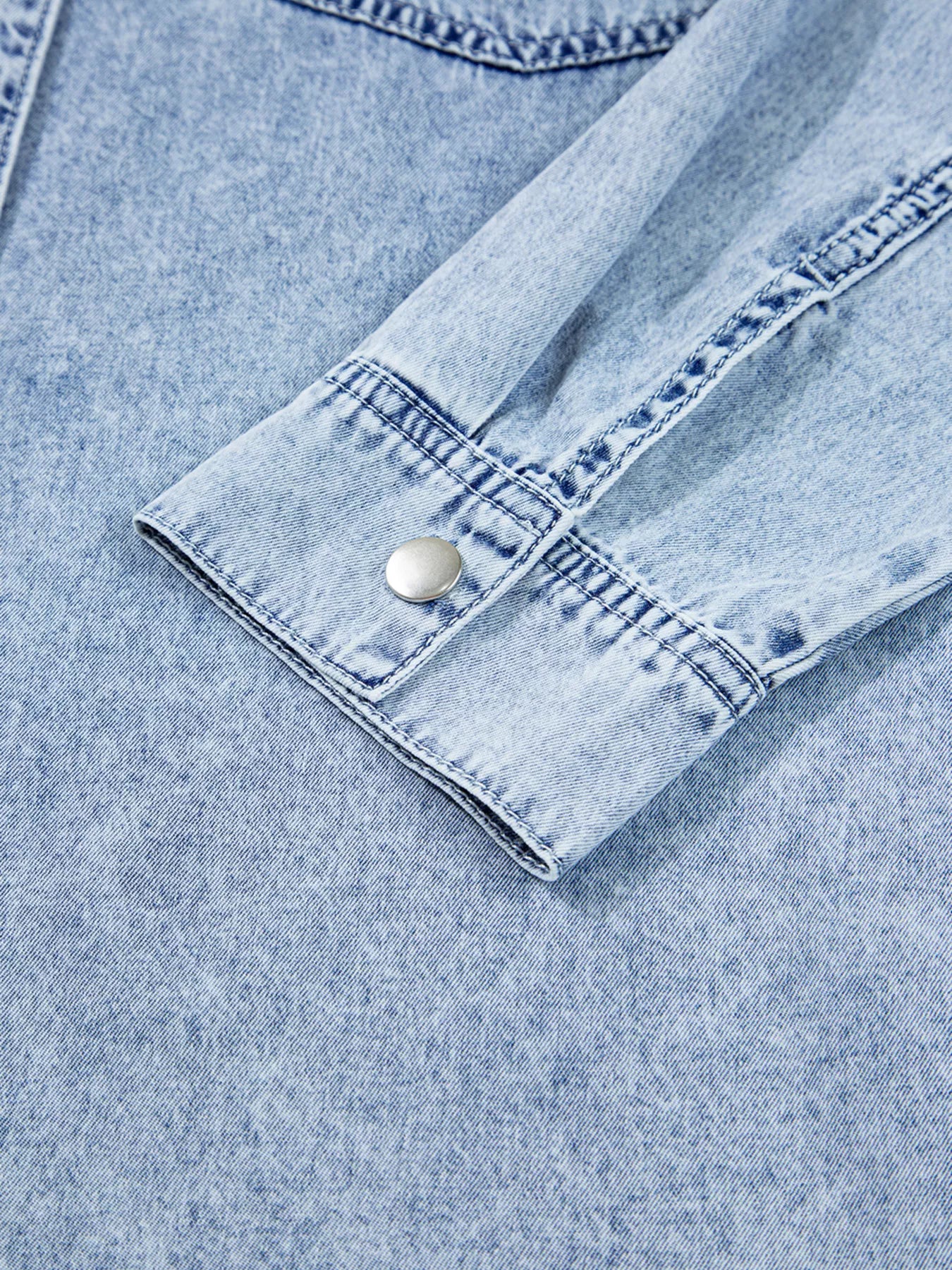 Close-up of a light blue denim shirt with a button on a matching fabric background