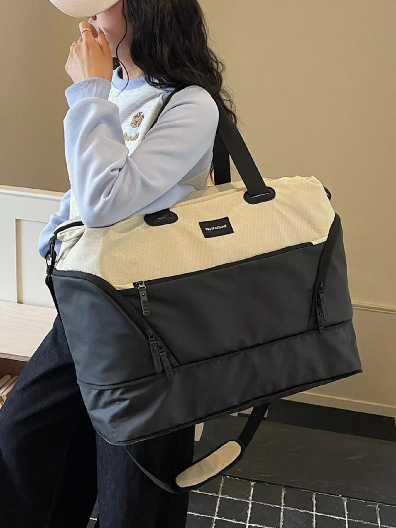 Person carrying a large black and beige bag indoors.
