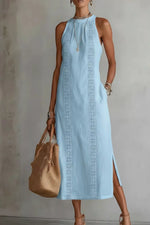 Woman wearing a light blue dress with intricate patterns, holding a beige handbag against a neutral background.