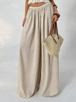 Person wearing beige wide-leg pants holding a woven bag on a plain background