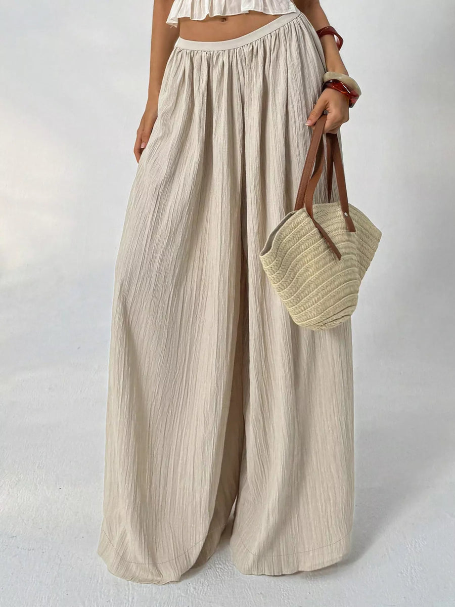 Person wearing beige wide-leg pants holding a woven bag on a plain background