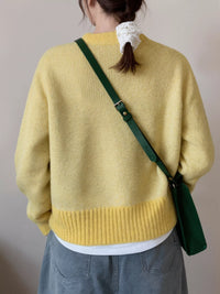 Person wearing a yellow sweater with a green crossbody bag over their shoulder against a plain background