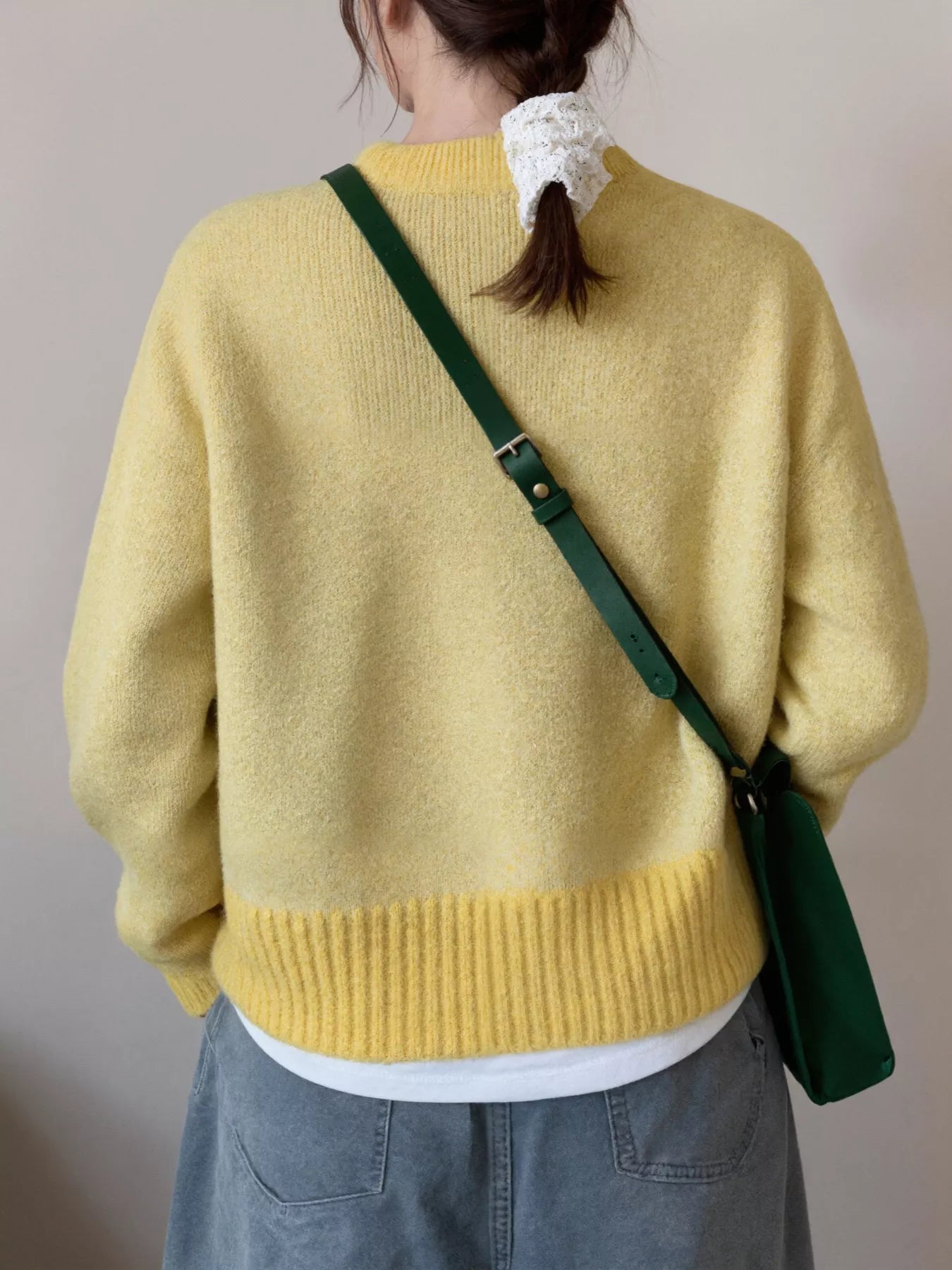 Person wearing a yellow sweater with a green crossbody bag over their shoulder against a plain background