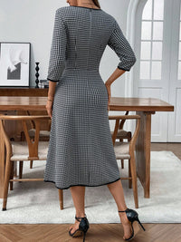 Woman wearing a black and white checkered dress in a dining room setting.