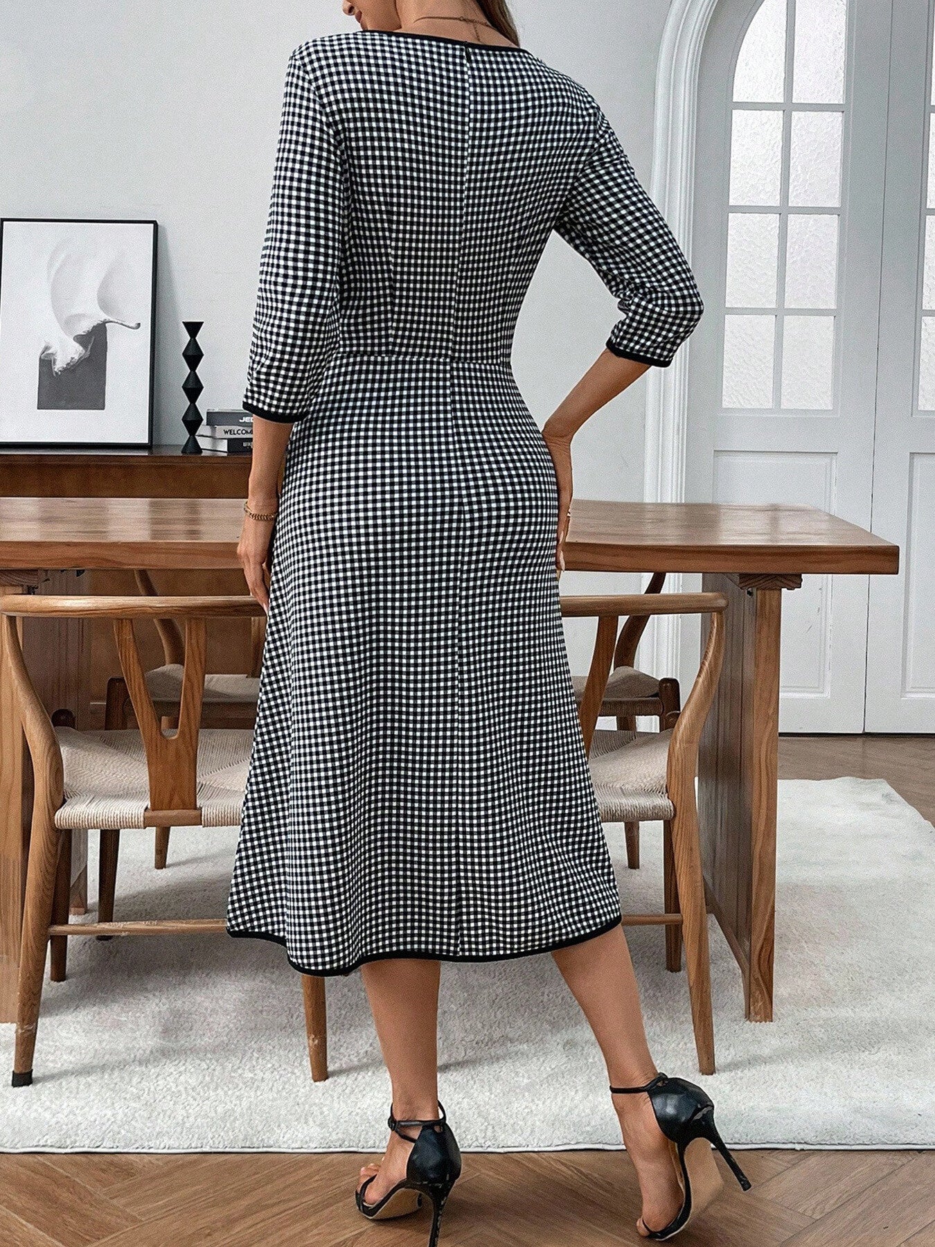 Woman wearing a black and white checkered dress in a dining room setting.