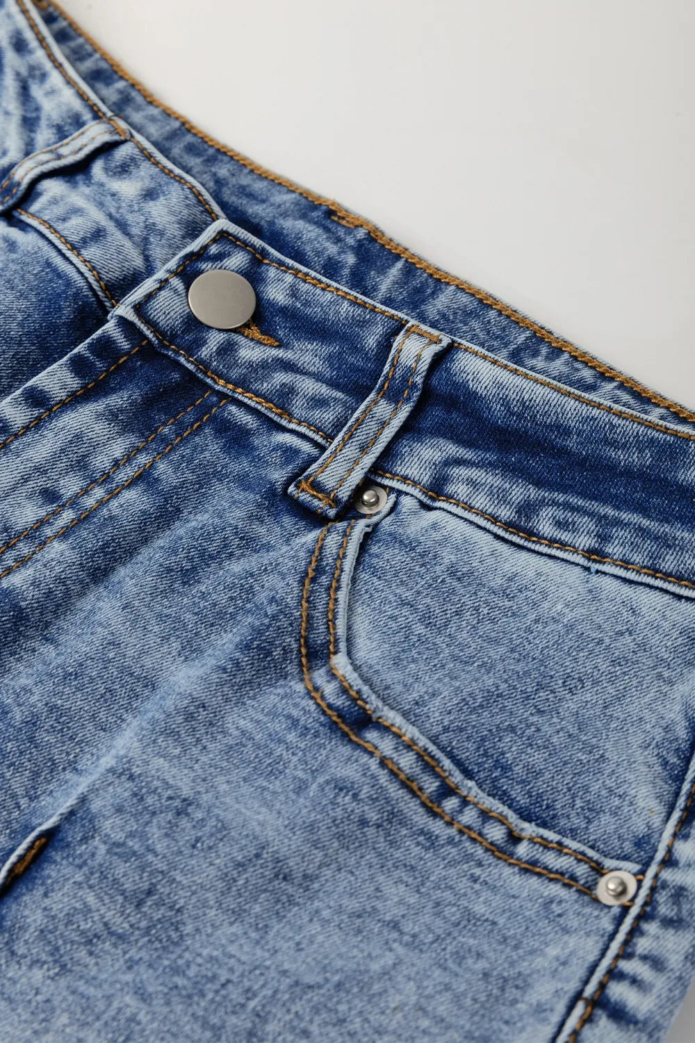 Close-up of blue denim fabric with a button and stitching detail.