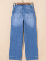 Blue jeans hanging on a wooden hanger against a beige background