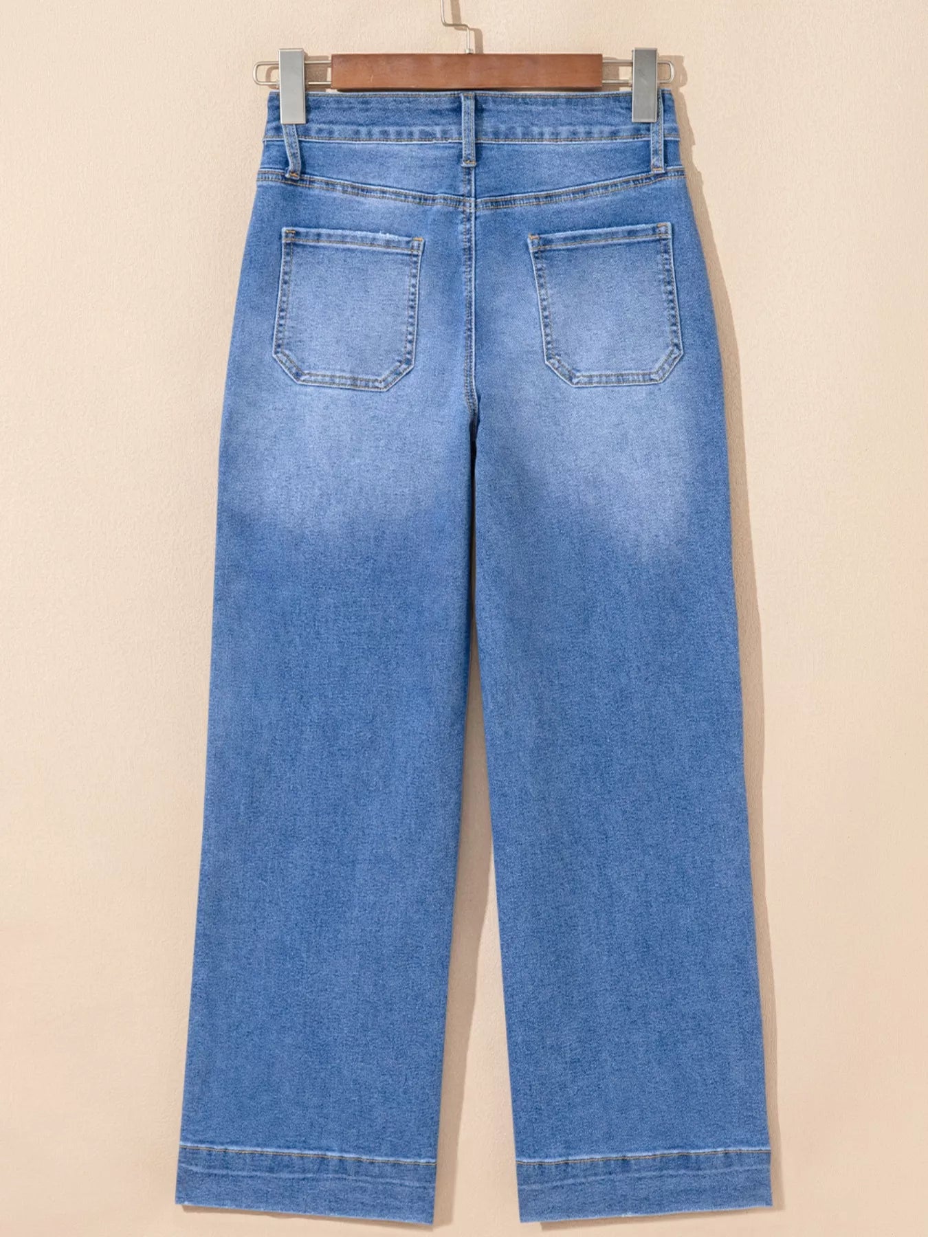 Blue jeans hanging on a wooden hanger against a beige background
