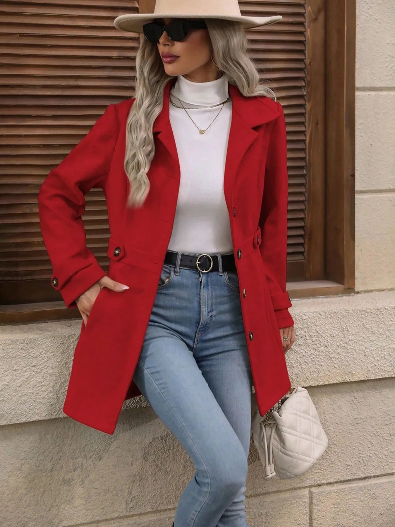 Woman wearing a red coat, white top, blue jeans, and beige hat against a wooden background.