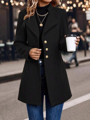 Person wearing a black coat with gold buttons, holding a coffee cup outdoors.