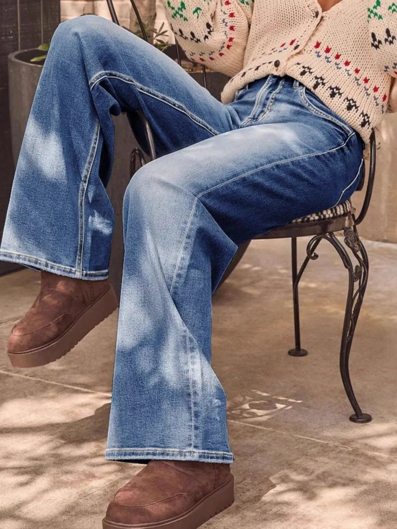 Person wearing blue jeans and brown shoes sitting on a chair.