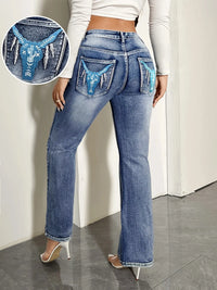 Person wearing blue jeans with lace detailing on the pockets against a white background