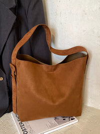 Brown leather tote bag on a surface with a coat and magazine in the background