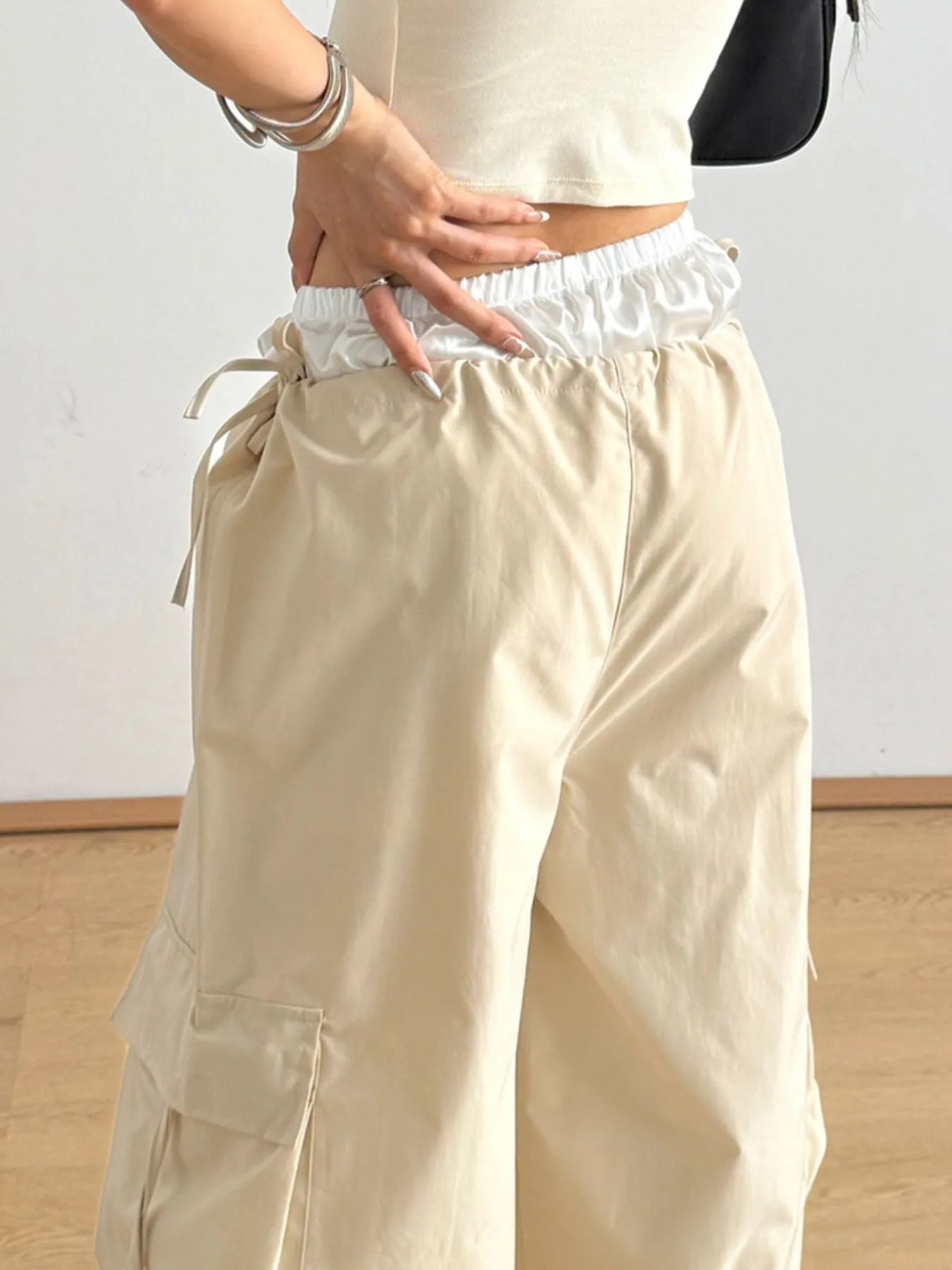 Person wearing beige cargo pants with a white top and black jacket on a plain background